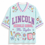 A light blue V-neck short-sleeve t-shirt with 'LINCOLN MIDDLE SCHOOL Ms. Taylor' printed on the front in purple and pink, decorated with school-themed doodles including a rainbow, pencil, flowers, and stars.