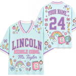 Front and back views of a light blue V-neck t-shirt with purple and pink lettering that reads 'LINCOLN MIDDLE SCHOOL Ms. Taylor' and 'YOUR NAME 24' on the back, decorated with cute school-themed illustrations like rainbows, pencils, apples, and books.