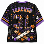 A black mesh short-sleeve jersey with purple trim, featuring 'TEACHER' and the number '31' in a Halloween-themed graphic filled with pumpkins, ghosts, bats, and stars. The sleeves have purple and orange stripes, and the back is decorated with spiderwebs, stars, and crossed pencils.