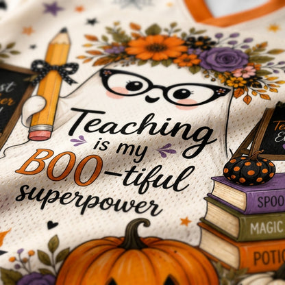 Close-up of a white mesh graphic print featuring a ghost illustration, floral crown, glasses, a pencil, stacked books, pumpkins, and the text 'Teaching is my BOO-tiful superpower'.