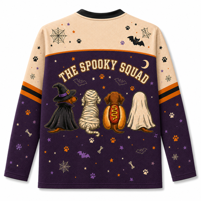 A long-sleeve crewneck sweatshirt shown from the back, featuring a Halloween-themed graphic with the text 'THE SPOOKY SQUAD' above four dogs dressed as a witch, mummy, hot dog, and ghost. The top half is beige with spiderwebs and paw prints, and the bottom half is dark purple with orange and purple accents.