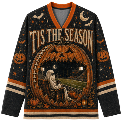 A long-sleeve V-neck sweater with a Halloween theme, featuring a large jack-o'-lantern with a football field and stadium scene inside, a ghost sitting in a chair, pumpkins, bats, stars, and the text 'TIS THE SEASON' on a black background with orange and beige accents.