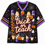A black short-sleeve V-neck t-shirt with a purple collar, featuring a Halloween-themed graphic print with the words 'trick or teach' in orange and white script. The design includes orange leopard-print pencils, jack-o'-lanterns, ghosts, bats, spiderwebs, and stars on a white background.