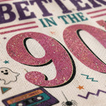 A close-up of a textured fabric print featuring a glittery pink '90' with retro Halloween graphics, including a cassette tape, spider, ghost, stars, and the text 'BETTER IN THE'.