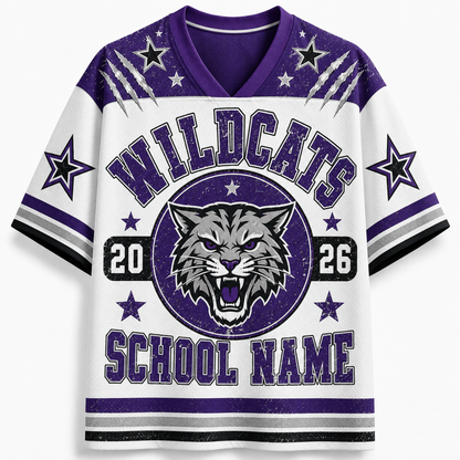 A white and purple short-sleeve V-neck jersey-style shirt with 'WILDCATS' across the chest, a wildcat head logo, numbers 20 and 26, and 'SCHOOL NAME' at the bottom, shown on a light gray background.