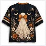 A black short-sleeve t-shirt with a graphic of a ghost in a cream lace dress and large orange bow, surrounded by orange and white flowers, bats, and leaves. The sleeves have orange and cream stripes.