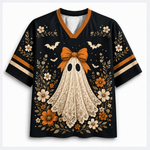 A black V-neck short-sleeve jersey-style shirt with an orange and cream Halloween graphic featuring a lace-textured ghost, orange bow, white bats, and cream and orange flowers, shown on a light gray background.