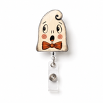 A Halloween-themed retractable badge reel featuring a cute, surprised cartoon ghost with a brown bow tie. The ghost has a light beige wood-grain finish with black eyes, eyebrows, and hair, pinkish-red cheeks, and a brown bow tie.
