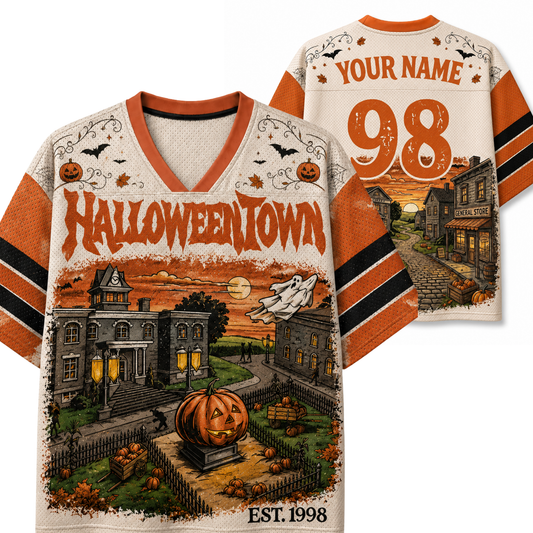 A custom Halloween-themed football jersey shown from both the front and back. The jersey features a cream-colored body with orange and black striped sleeves, a V-neck collar, and a detailed graphic of a haunted house, a jack-o'-lantern, a ghost, and spooky town buildings.