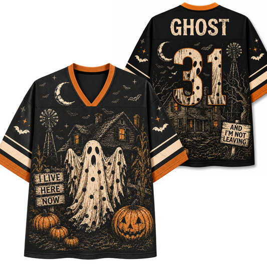 A black V-neck football-style jersey shown from the front and back, featuring a Halloween graphic with a ghost, haunted house, pumpkins, bats, moon, and windmill. The front reads 'I LIVE HERE NOW' and the back reads 'GHOST 31 AND I'M NOT LEAVING'.