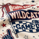Close-up of a white athletic jersey fabric printed with a red, white, and navy blue 'Wildcats Game Day' graphic, including a pennant, stars, and a foam finger.