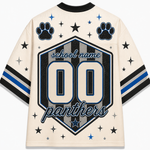 A cream-colored short-sleeve jersey shown from the back, featuring a large black, gray, and blue shield graphic with the text 'school name', '00', and 'panthers'. The jersey is decorated with black paw prints, stars, and blue and black stripes on the sleeves.