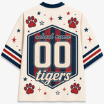 A cream-colored mesh short-sleeve jersey shown from the back, featuring a large navy and red hexagonal graphic with the text 'school name', '00', and 'tigers'. The design is decorated with red paw prints, red and navy stars, and red and navy stripes on the sleeves.