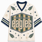 A cream-colored mesh sports jersey with navy blue trim, featuring a large central shield graphic with the word 'eagles' in cream lettering over green and tan vertical stripes. The sleeves have navy and green stripes, and the front is decorated with navy and green eagle wings and stars.