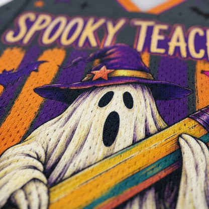 Close-up of a Halloween-themed sports jersey featuring a cartoon ghost in a purple witch hat with a star, holding a rainbow-striped bat, with the text 'SPOOKY TEACH' on a dark background with orange bat silhouettes.