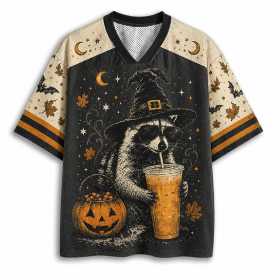A short-sleeve V-neck t-shirt featuring a Halloween-themed graphic print of a raccoon in a witch hat holding an iced drink next to a jack-o'-lantern, with beige sleeves and a black body.