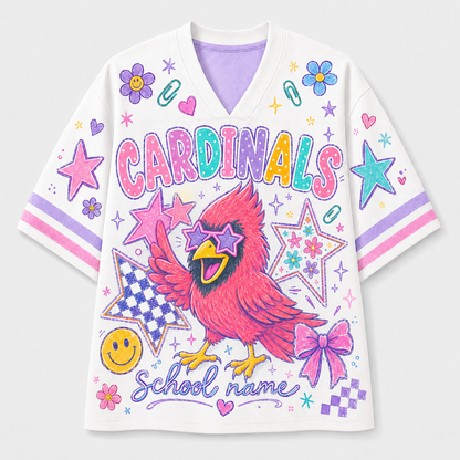 A white V-neck short-sleeve jersey-style top with colorful school-themed graphics, including the word 'CARDINALS,' a red cardinal, stars, bows, smiley faces, and 'School name' text, shown on a light gray background.
