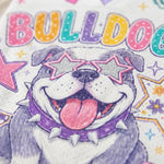 Close-up of a printed graphic featuring a bulldog with star-shaped sunglasses, a purple spiked collar, and colorful 'BULLDOG' lettering on a white textured background.