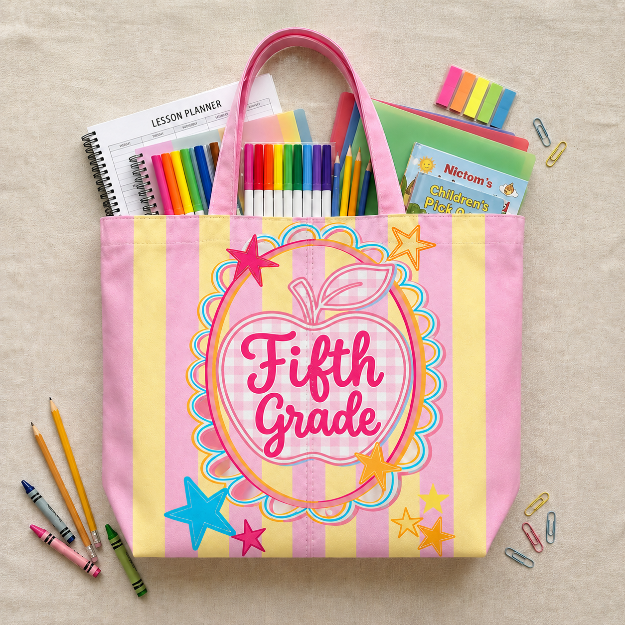 Pink tote bag with 'Fifth Grade' design filled with school supplies on a beige background