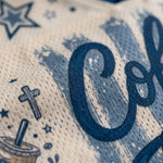 Close-up of a cream-colored mesh fabric with a blue distressed graphic print featuring the letters 'Co', stars, a coffee cup, and a cross.