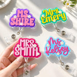 Four colorful name badge holders with names 'MS SHIRE', 'Mrs Emery', 'Mrs Smith', and 'Mrs Kelsey' on a light background.