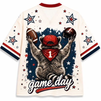 A cream-colored athletic jersey with a graphic of a raccoon holding a football and a helmet, wearing a red bandana with the number 1. The jersey features 'game day' written across the bottom and is decorated with red, white, and blue stars and stripes.