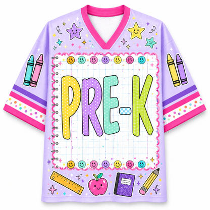A light purple short-sleeve V-neck jersey-style shirt with a colorful school-themed graphic. The front features the word 'PRE-K' in large pastel letters inside a notebook-style border, surrounded by smiley faces, crayons, stars, a ruler, an apple, and other school supplies.