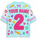 A light blue short-sleeve t-shirt with customizable graphics, featuring a large pink number '2' and the text 'YOUR NAME' on the back, surrounded by colorful cartoon flowers, stars, hearts, bows, and pencils.
