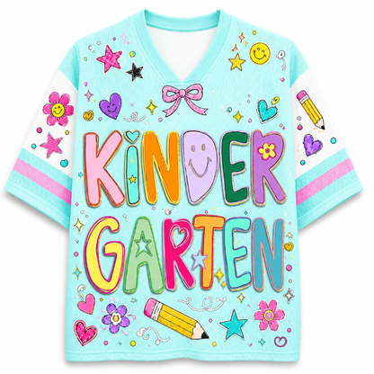 A light blue V-neck short-sleeve t-shirt with 'KINDER GARTEN' printed in large, colorful cartoon letters. The shirt is decorated with playful school-themed graphics including stars, flowers, hearts, smiley faces, and a pencil on a plain white background.