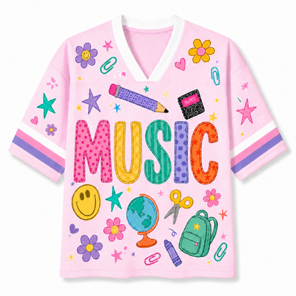 A pink short-sleeve V-neck t-shirt featuring a colorful 'MUSIC' graphic and school-themed illustrations including flowers, smiley faces, scissors, a globe, a backpack, and paperclips on a white background.
