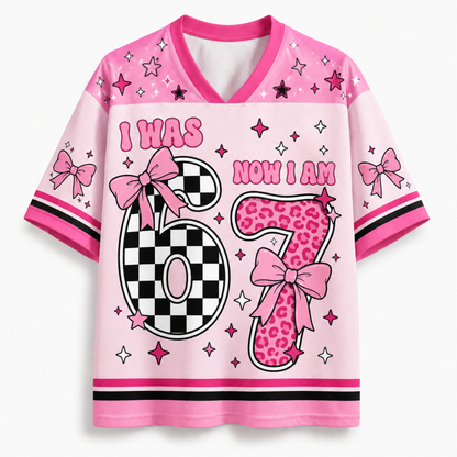 A pink short-sleeve V-neck t-shirt with a 'I WAS NOW I AM 6' birthday graphic. The number 6 is split into a black-and-white checkerboard pattern on the left and a pink leopard print pattern on the right, decorated with pink bows.