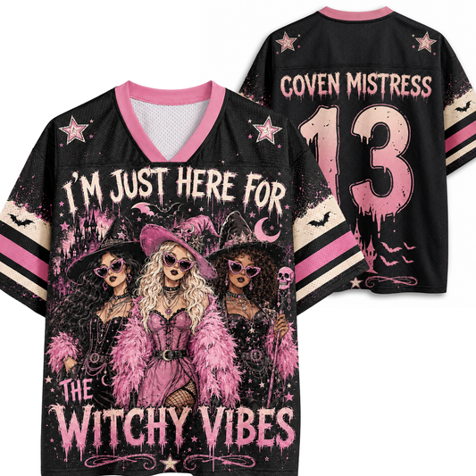 Black V-neck graphic jersey shown from front and back on a white background. The front features pink and beige witch illustrations with the text 'I'M JUST HERE FOR THE WITCHY VIBES'.