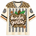 A short-sleeve V-neck jersey-style shirt with a cream mesh base, leopard-print shoulder panels, black-and-white checkered stripes, and a large central apple graphic with the words 'kinder garten' in script over a leopard print background. Decorative stars and pineapple motifs appear on the sleeves.