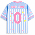Back view of a customizable short-sleeve jersey in light blue and white vertical stripes, featuring a large pink number 0, 'YOUR NAME' text, and pink, yellow, and white graphic accents.