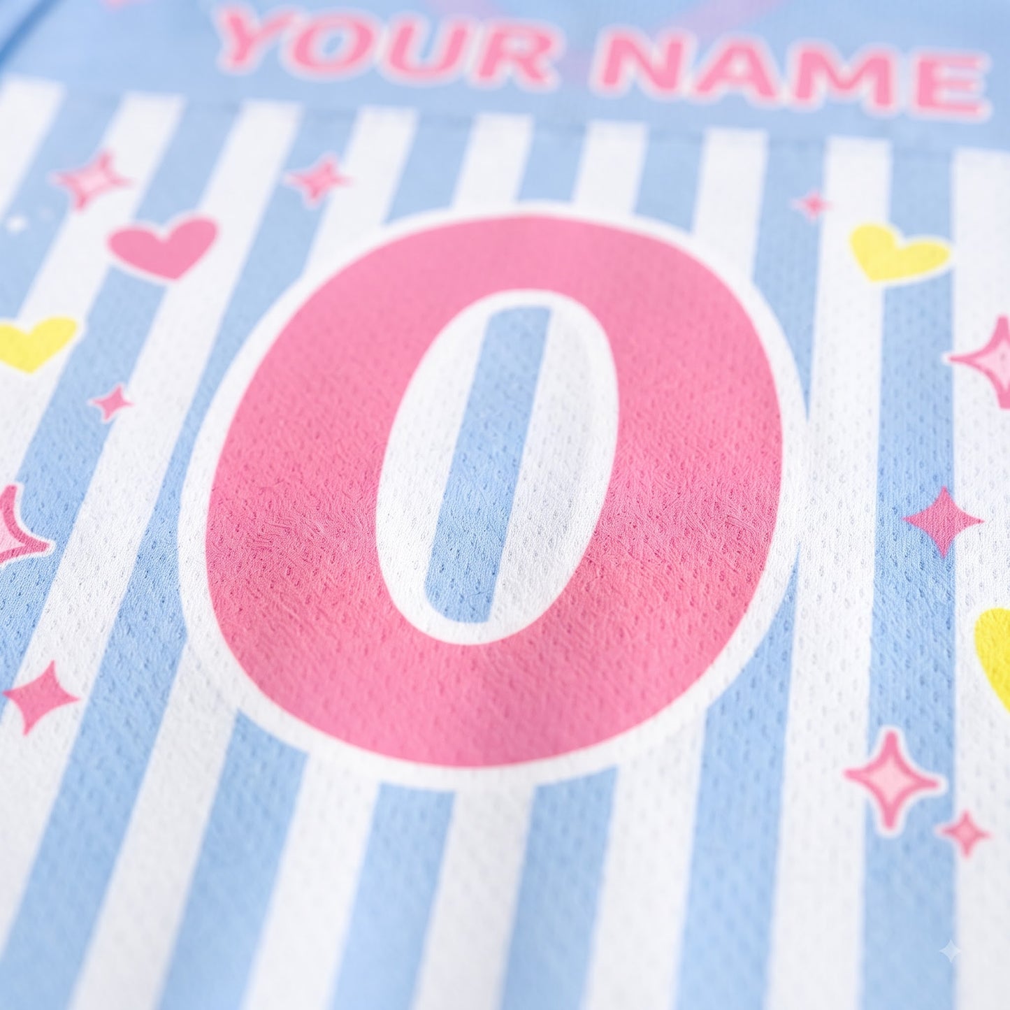 Close-up of a personalized sports jersey fabric with light blue and white vertical stripes, a large pink number zero, and pink, yellow, and pink star heart graphics. The text 'YOUR NAME' is partially visible at the top.