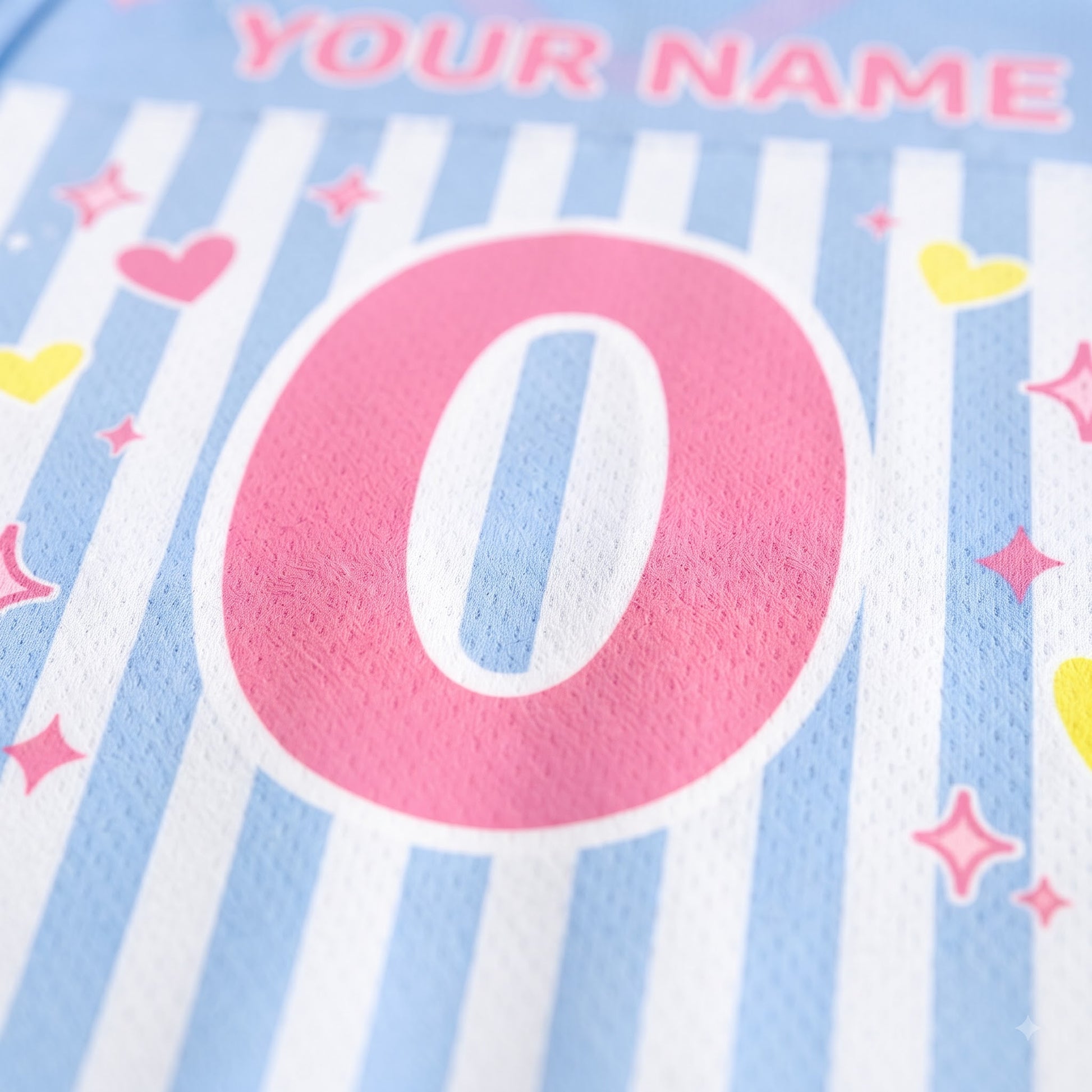Close-up of a personalized sports jersey fabric with light blue and white vertical stripes, a large pink number zero, and pink, yellow, and pink star heart graphics. The text 'YOUR NAME' is partially visible at the top.