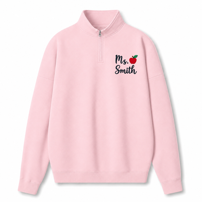 A light pink quarter-zip sweatshirt with 'Ms. Smith' and a small red apple graphic printed on the left chest, displayed on a clean white background.