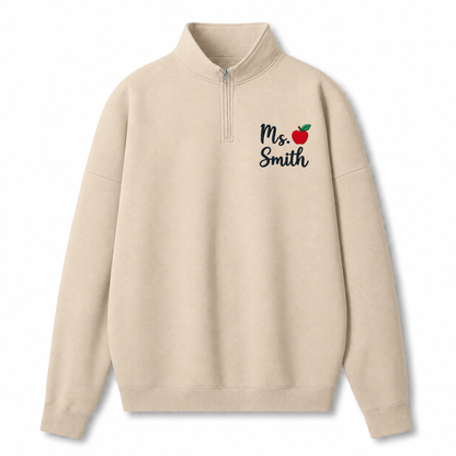 A beige quarter-zip sweatshirt with 'Ms. Smith' and a small red apple graphic printed on the left chest, displayed on a clean white background.