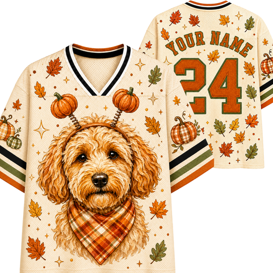 A cream-colored custom sports jersey shown from both front and back, featuring a cartoon dog wearing a plaid bandana and antlers, surrounded by autumn leaves, pumpkins, and stars. The front has a V-neck with black, white, and orange trim, and the back displays 'YOUR NAME' and the number '24' in orange and green.