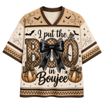 A short-sleeve V-neck t-shirt with a Halloween-themed graphic print. The design features the text 'I put the BOO in Boujee' with 'BOO' styled in a checkered pattern, a large black bow, and two pumpkins with leopard-print bows.