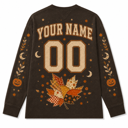 A dark brown long-sleeve t-shirt with a custom Halloween-themed graphic on the back. The design features a customizable name and number '00' in a distressed beige font, surrounded by autumn leaves, pumpkins, stars, and crescent moons in orange, beige, and brown tones.