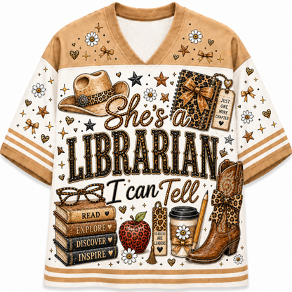 A short-sleeve V-neck t-shirt with a western-themed librarian graphic print. The design features a brown and cream color scheme with illustrations of a cowboy hat, a leather-bound book, a stack of books, an apple, a coffee cup, and the text 'She's a LIBRARIAN I can Tell'.