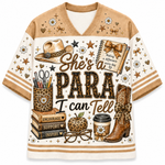 A women's V-neck athletic-style T-shirt with tan shoulder panels and striped sleeve cuffs, featuring a large western-themed graphic on the front. The design includes a cowboy hat, boots, books, flowers, stars, and the text 'She's a PARA I can Tell' in brown and black lettering.