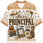 A women's short-sleeve V-neck t-shirt with a western-themed graphic print. The design features a tan and cream color-blocked style with a large central text graphic reading 'She's a PRINCIPAL I can Tell' surrounded by illustrations of a leopard-print cowboy hat, books, an apple, keys, a coffee cup, and a cowboy boot.