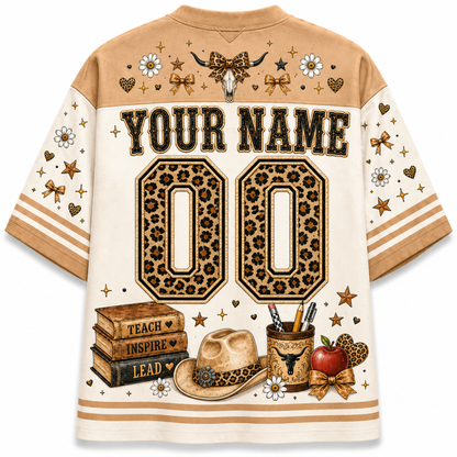 A short-sleeve custom sports jersey shirt shown from the back, featuring a tan and cream color scheme with leopard-print details, western-themed graphics including a cowboy hat, books, an apple, and a skull, and placeholder text 'YOUR NAME' and '00'.