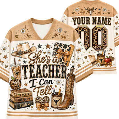 A custom-designed v-neck football-style shirt shown from both front and back. The design features a tan and cream color scheme with leopard print accents, decorated with school and teaching-themed illustrations including a cowboy hat, boots, books, an apple, and a notebook.