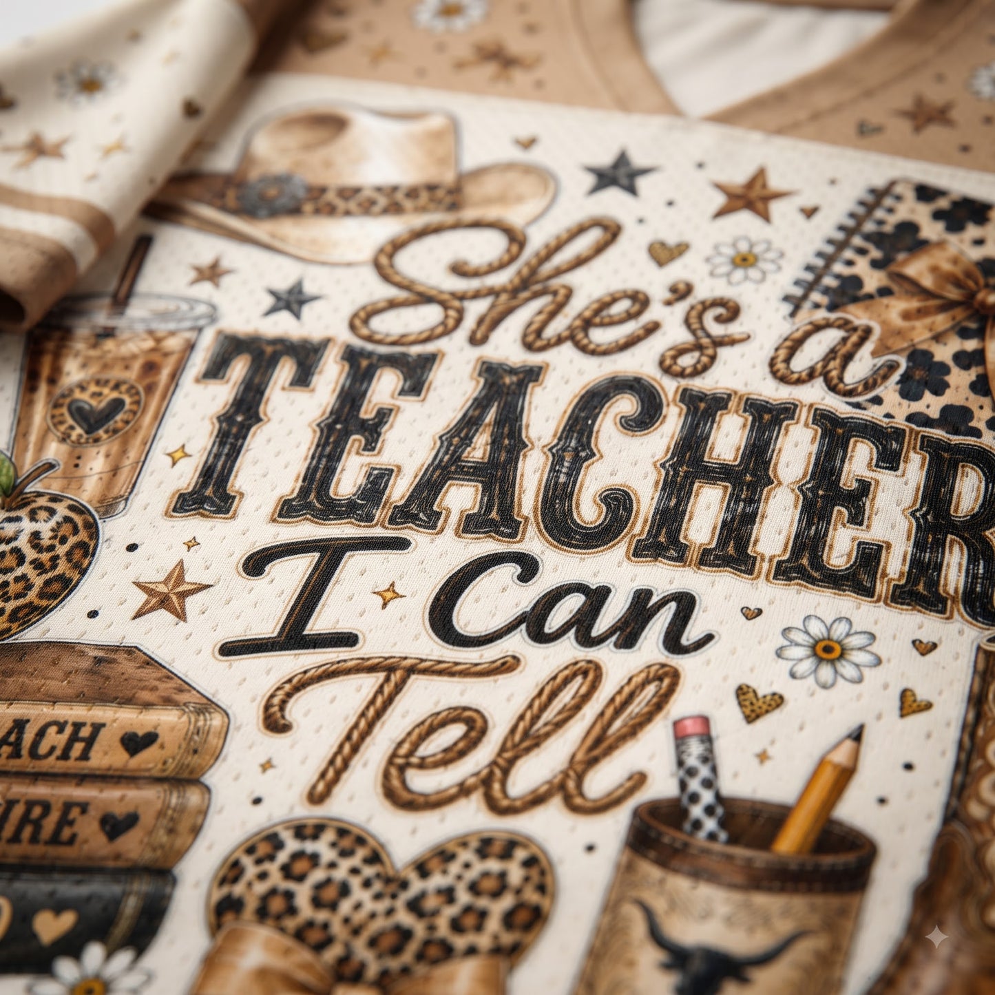 A close-up of a western-themed printed design with the phrase “She’s a TEACHER I Can Tell” in large decorative lettering. The artwork includes a cowboy hat, stars, flowers, a pencil cup, books, and leopard-print accents on a warm cream background.