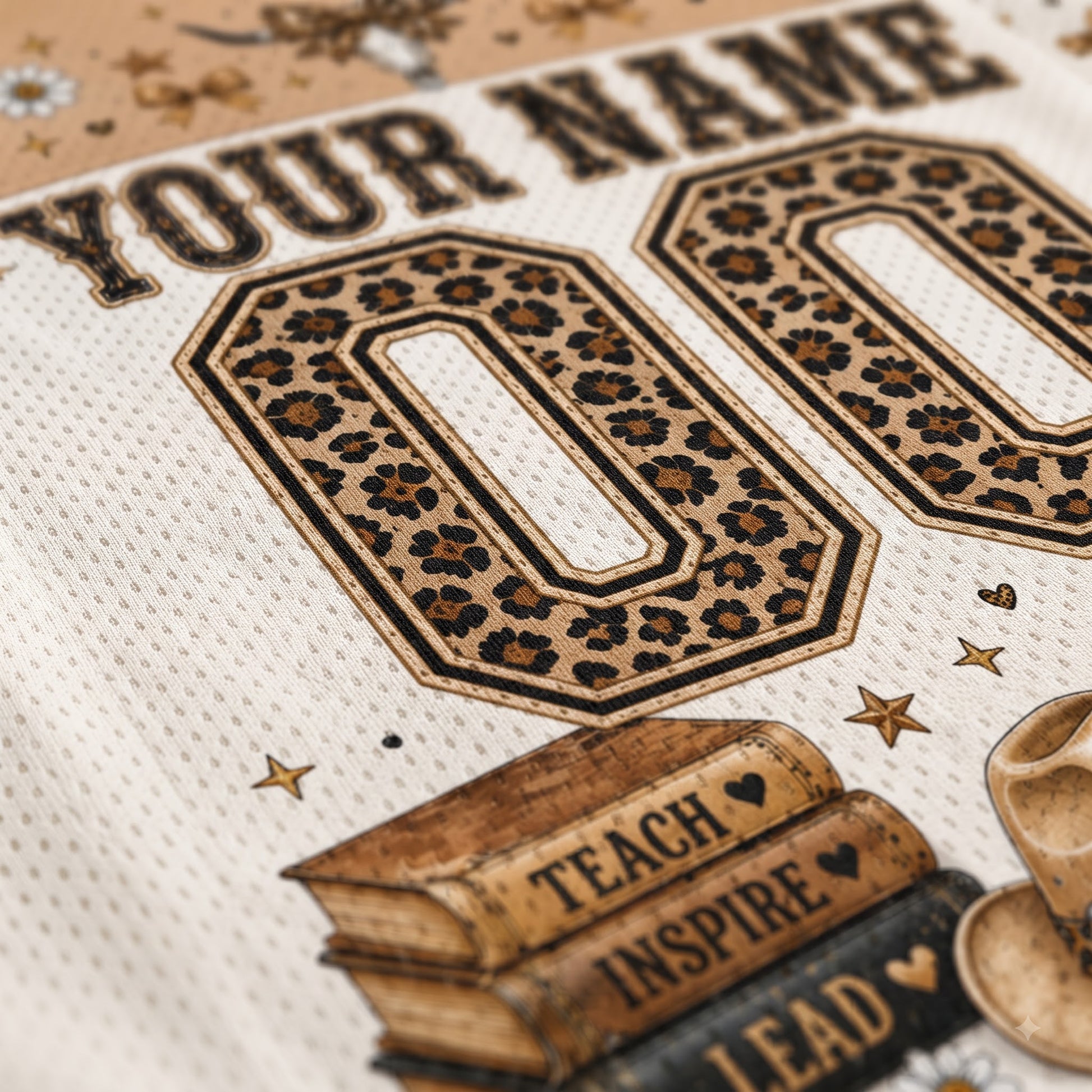 Close-up of a custom sports jersey print featuring leopard-print '00' numbers, 'YOUR NAME' text, stars, books with 'TEACH INSPIRE LEAD', and a cowboy hat on an off-white mesh fabric.