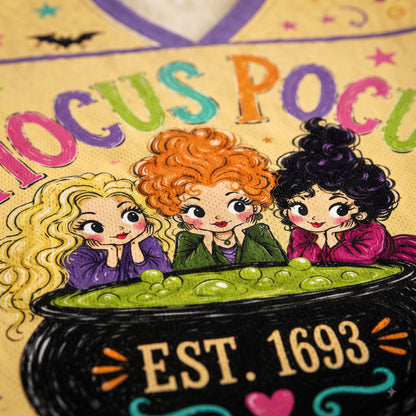 A close-up of a colorful illustrated fabric or print featuring three cartoon witch sisters behind a cauldron with green potion and the text 'FOCUS POCAU' and 'EST. 1693'.
