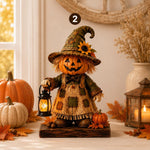 A decorative autumn scarecrow figurine stands on a wooden base in a styled indoor setting. The scarecrow has a carved pumpkin face, a tall camouflage-patterned hat with a sunflower accent, straw hair, and a patchwork-style dress, while holding a small lantern.